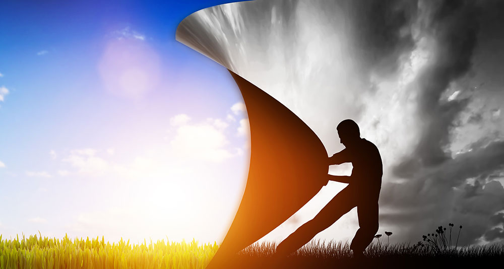 Man turning the page on a black and white, cloudy day to reveal sunny, blue skies