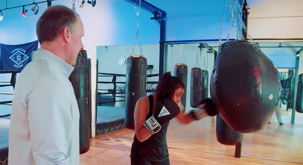 Boxing gym owner looks on as a young woman punches a bag