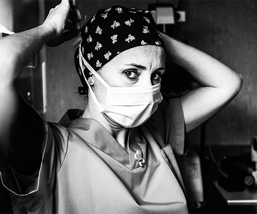 black and white image of a serious-looking nurse putting on her facemask to prepare for surgery
