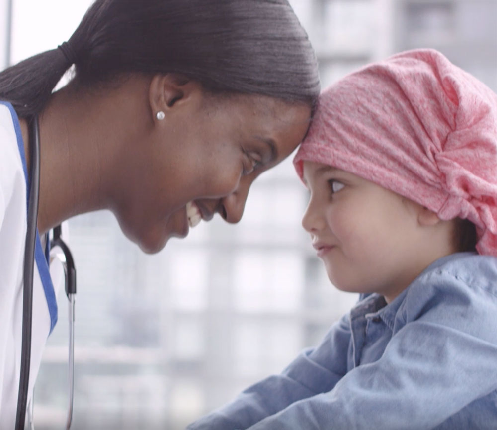 Female nurse and young girl, heads pressed together and looking at each other; healthcare video marketing